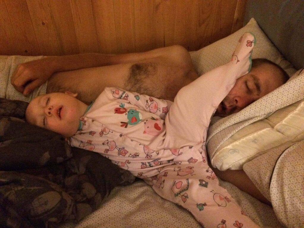 Young child asleep in starfish position with foot on dad's head