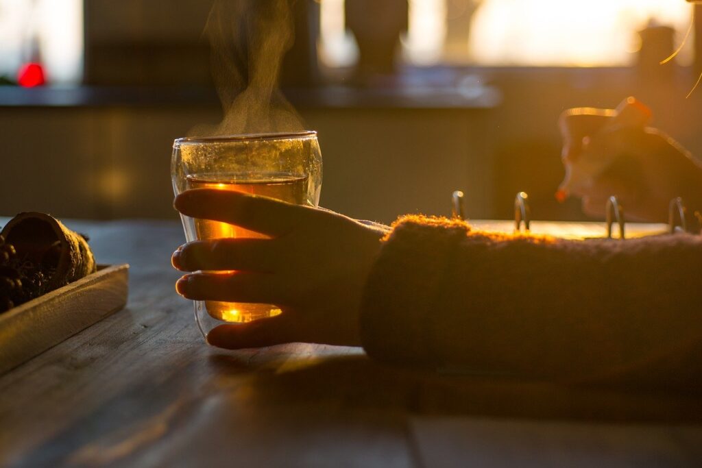 Steaming hot cup of tea in woman's hands with soft light streaming through window