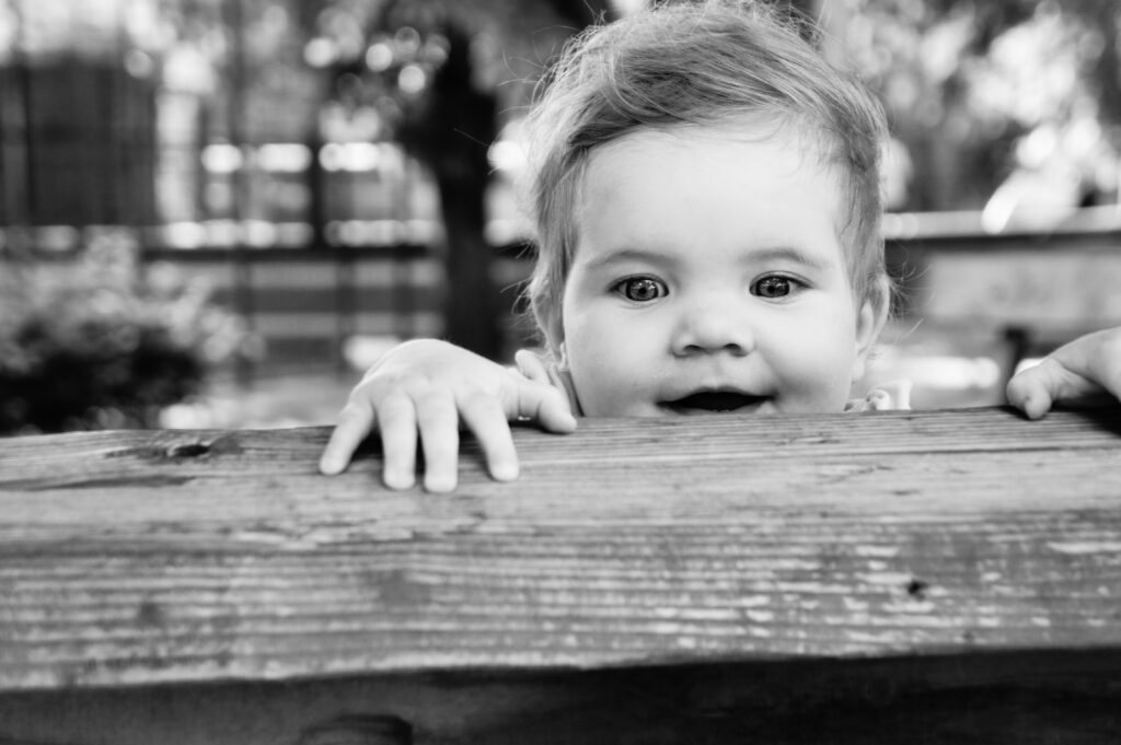 Curious toddler peering over wooden ledge with look of amazement on her face, black and white photo